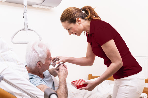 Pflegekraft unterstützt älteren Herren beim Trinken